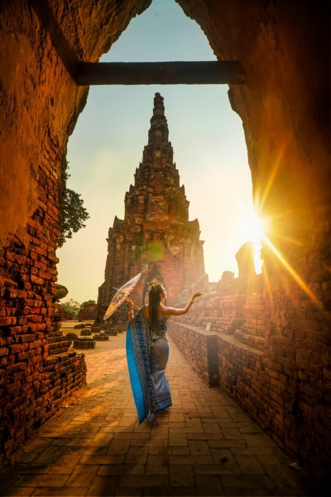 pexels-photo-2070485-2070485 A woman in traditional wear stands with an umbrella at a historic Ayutthaya temple during sunset.